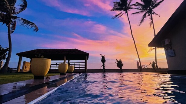 Ein Pool mit Sonnenuntergangsblick, Palmen und einer überdachten Sitzgelegenheit.