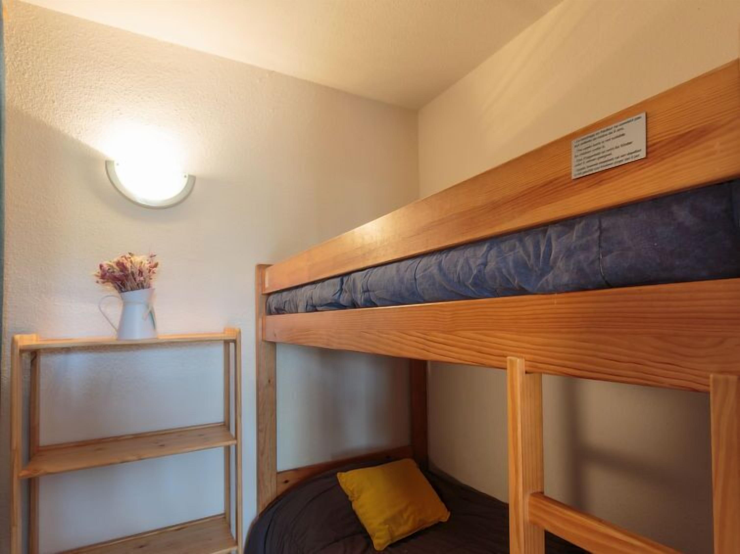 Een slaapkamer met stapelbed, een lamp boven het bed en een tafeltje met een vaas.