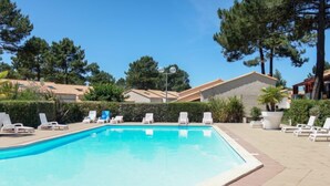 Ein rechteckiger Swimmingpool mit klarem, blauem Wasser, umgeben von weißen Liegestühlen und Topfpflanzen.