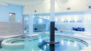 A modern indoor pool area with a central water feature, seating areas, and a clear view of the pool's edge. - Pooches Paradise - Pet Friendly Hot Tub & Pool (Canmore)