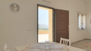 Ein Zimmer mit gedecktem Tisch für zwei Personen, einer Uhr an der Wand und einer Tür zu einem Außenbereich mit Landschaftsblick.