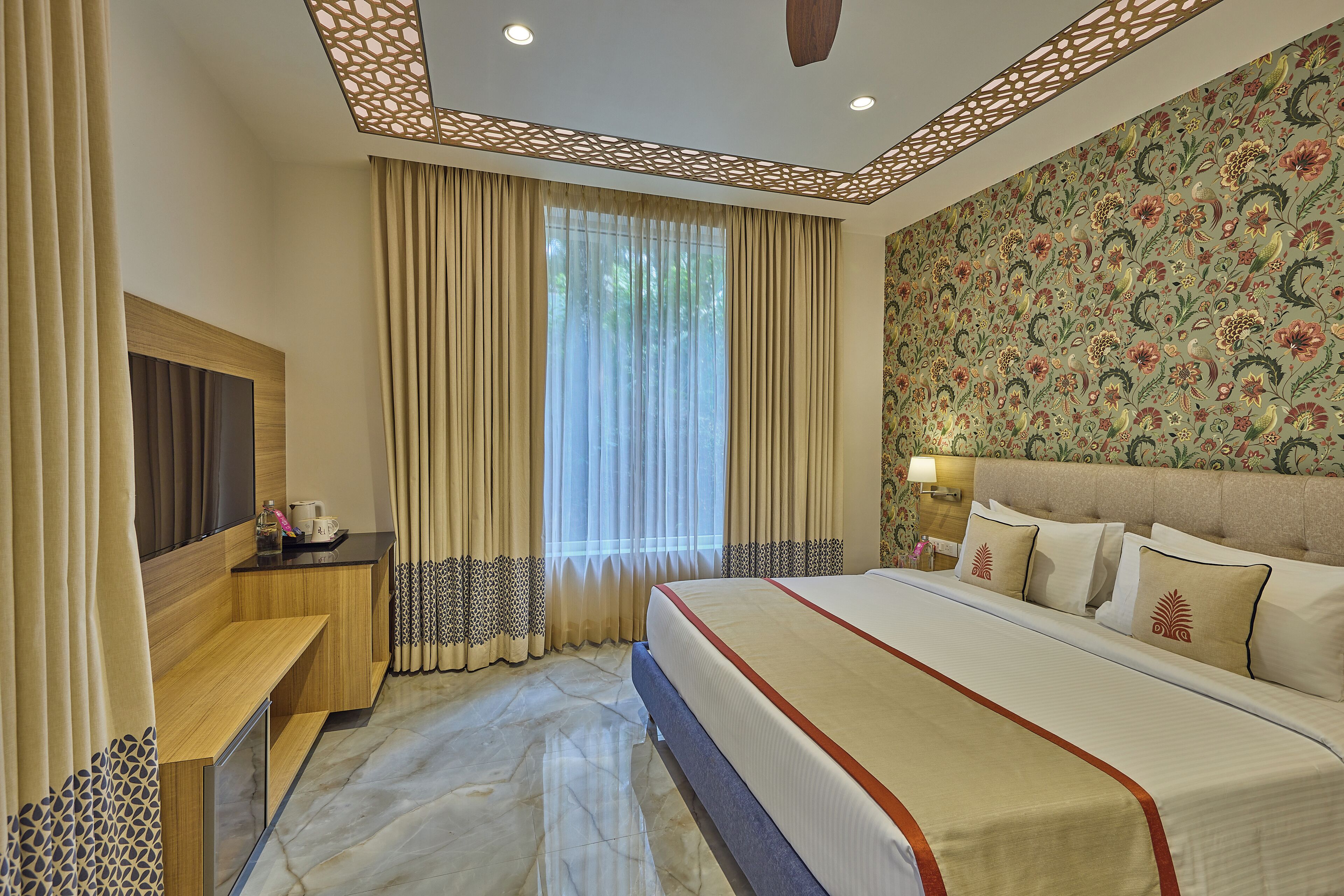 Quarto de hotel com uma cama grande, televisão, mesa de cabeceira e janela com cortinas.