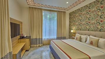 Quarto de hotel com uma cama grande, televisão, mesa de cabeceira e janela com cortinas.