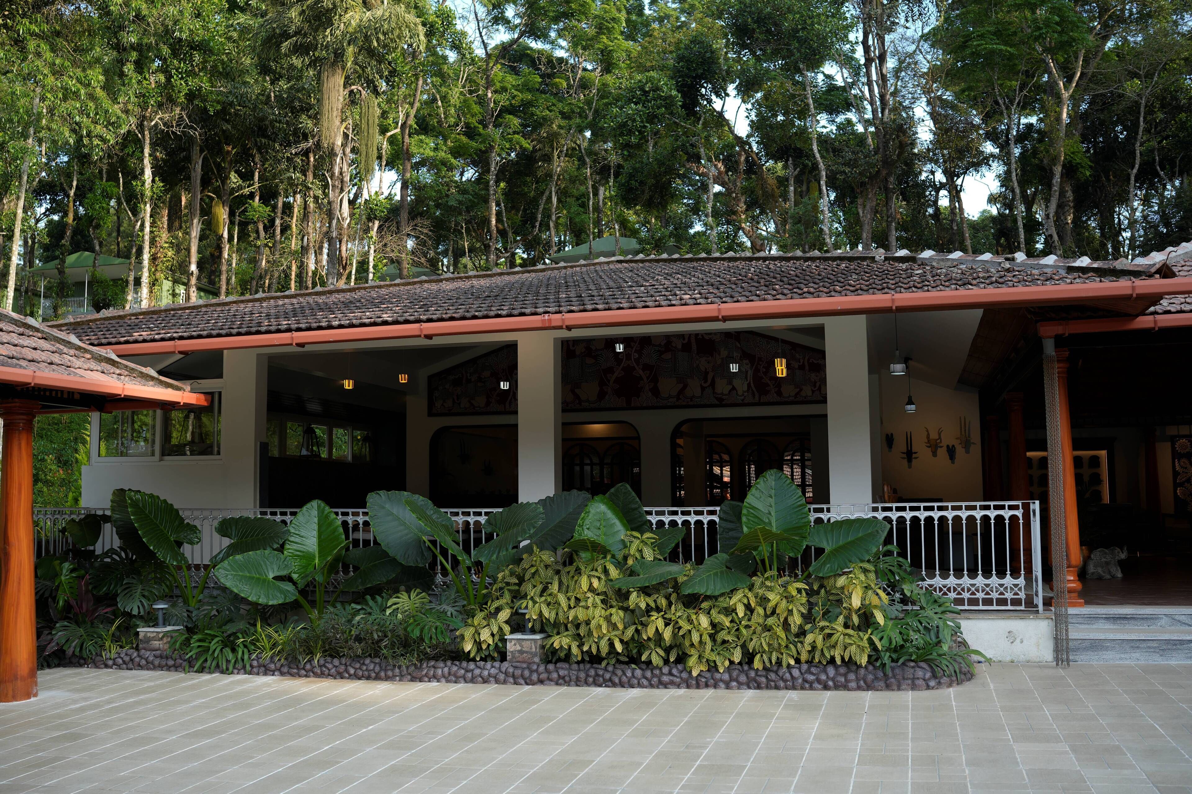 A covered outdoor area with a tiled floor, surrounded by large tropical plants and a stone pathway.