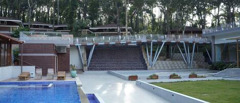 Una piscina con un deck blanco, un puente y vistas a un área boscosa.