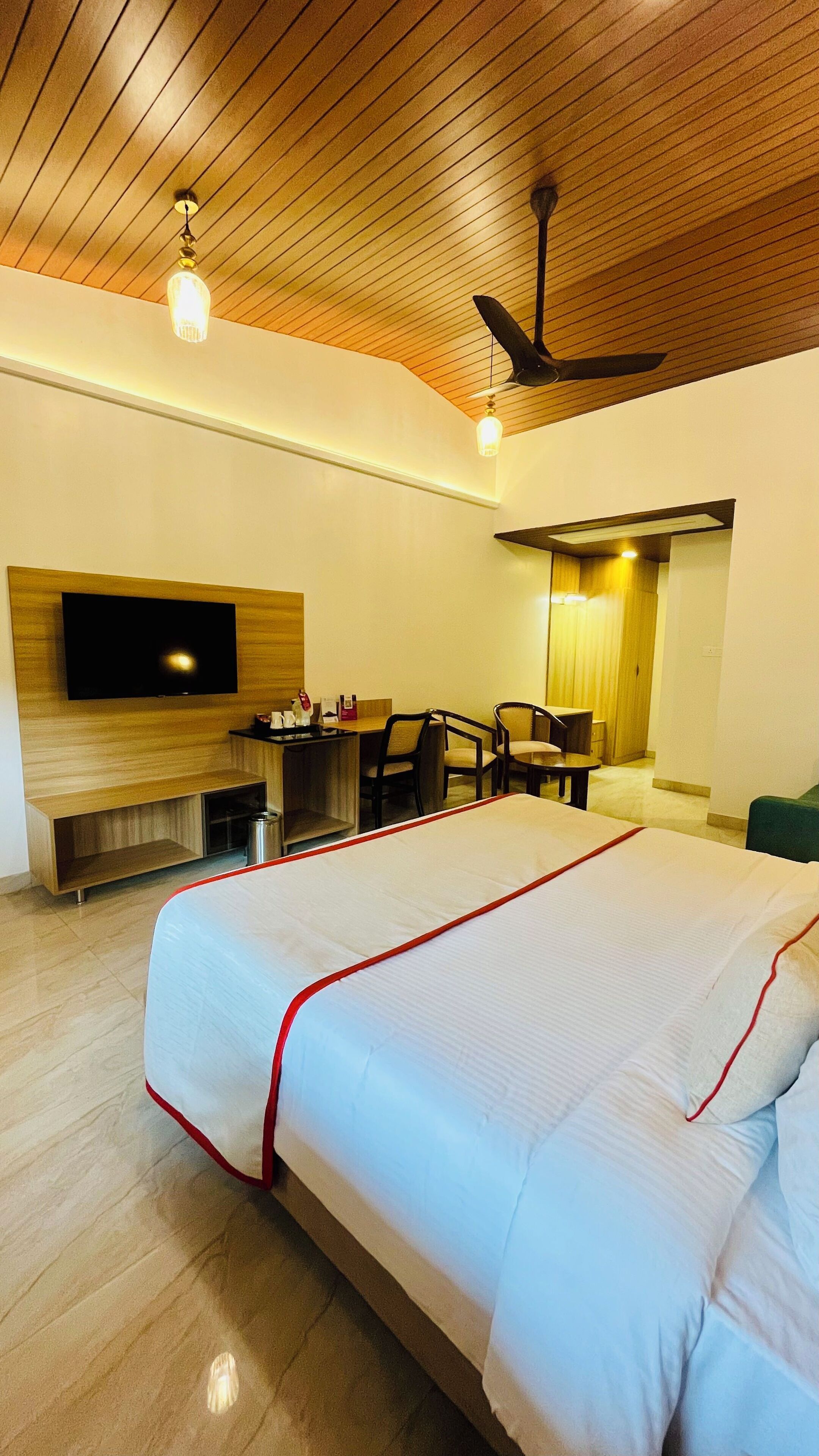 A hotel room with a large bed, a desk with chairs, a television, and a ceiling fan.