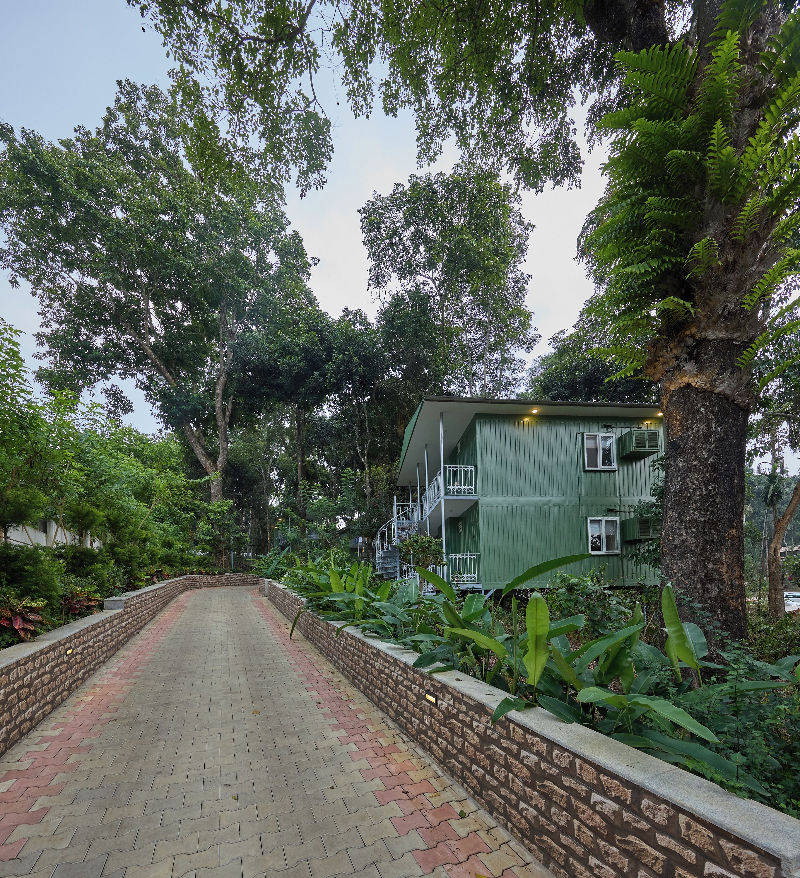 A pathway leading to a green building with a brick wall and a staircase.