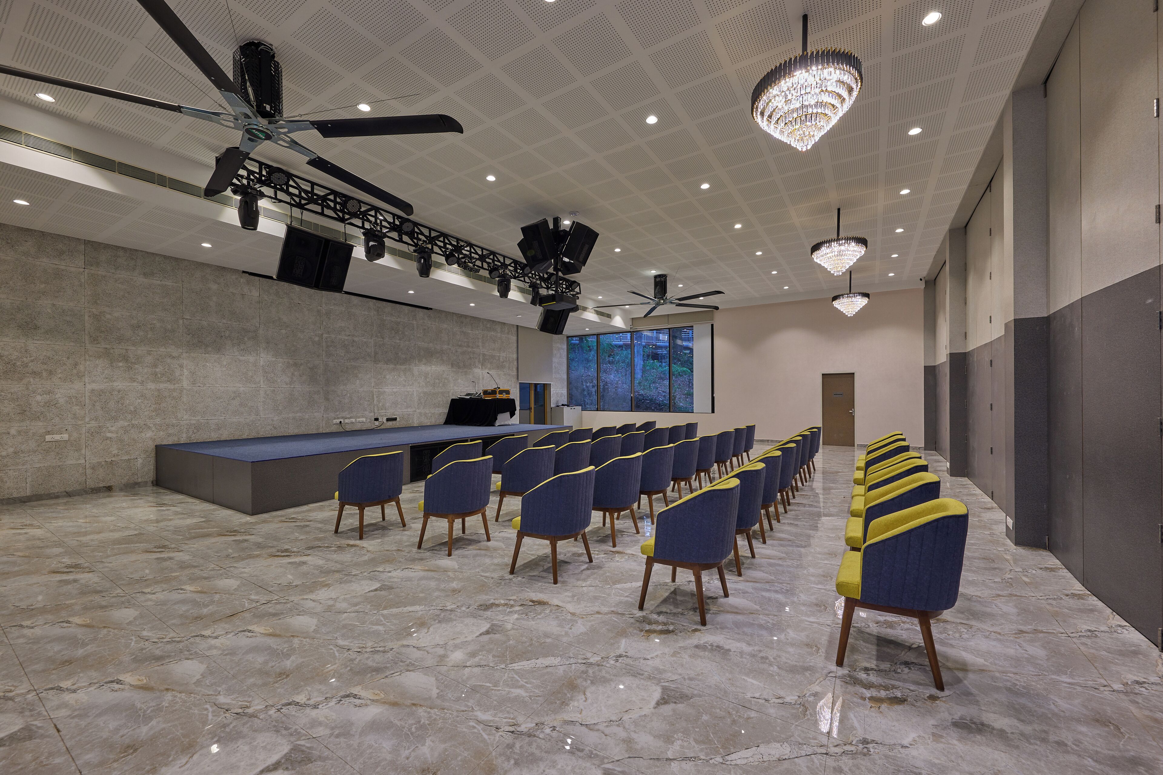 A conference room with a long table, rows of chairs, ceiling fans, and chandeliers.