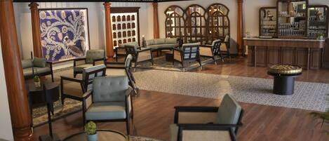 Eine großzügige Lobby mit hoher Decke, Holzböden und verschiedenen Sitzgelegenheiten, darunter Sofas und Sessel. Eine große Wanddekoration und ein Barbereich mit Regalen sind ebenfalls vorhanden.