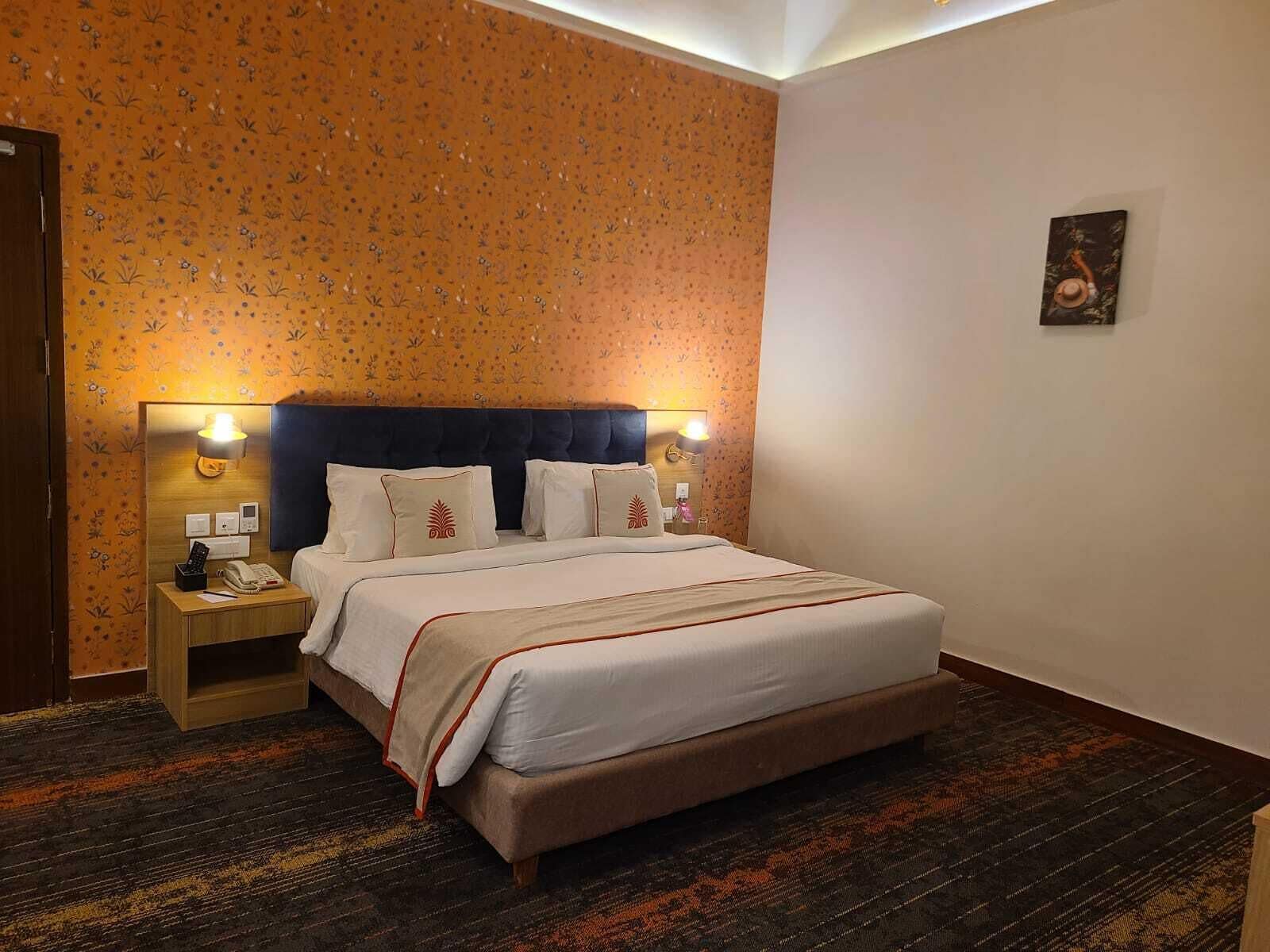 Une chambre d’hôtel avec un grand lit, une table de chevet avec un téléphone et un mur orné d’un motif floral.