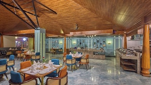 A spacious restaurant with high ceilings, wooden beams, and a polished marble floor. Tables are set with blue chairs and white tableware. - Regenta Resort Sakleshpur (Sakleshpur)