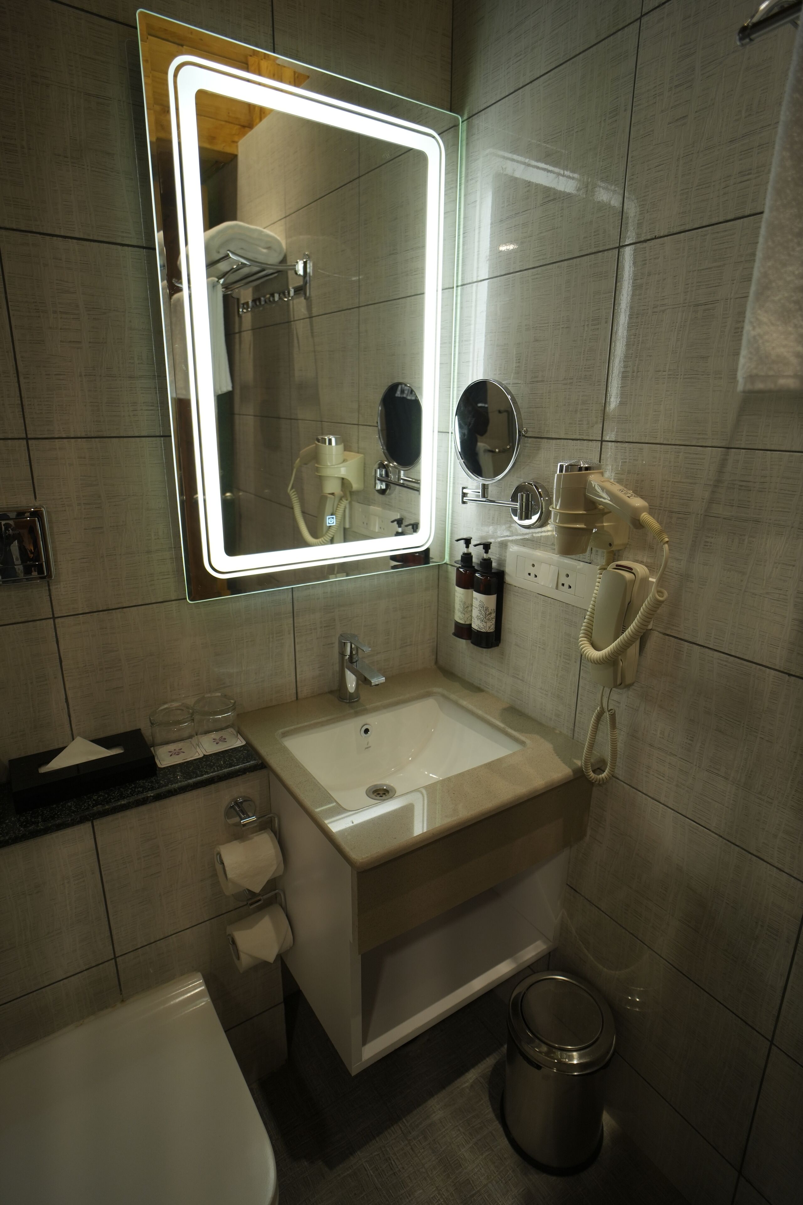 A modern bathroom with a large mirror, a sink, a toilet, and a trash can.