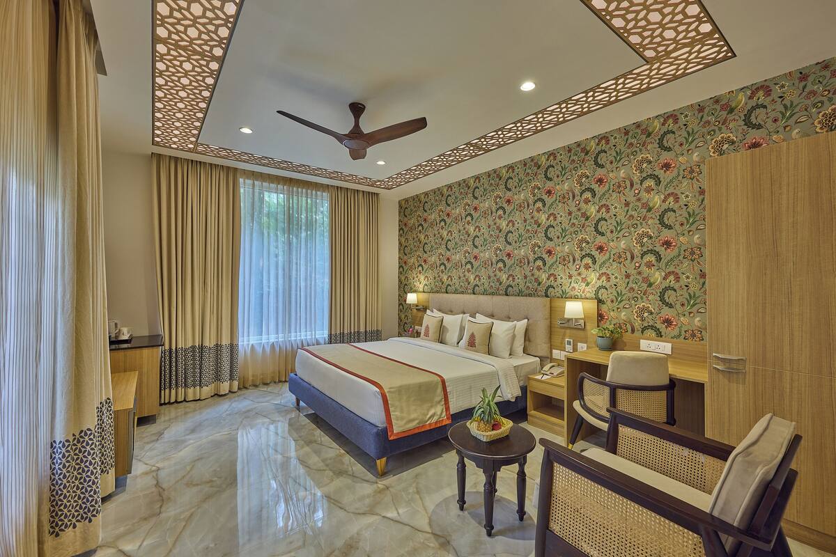 A hotel room with a large bed, a desk, a chair, and a small table.