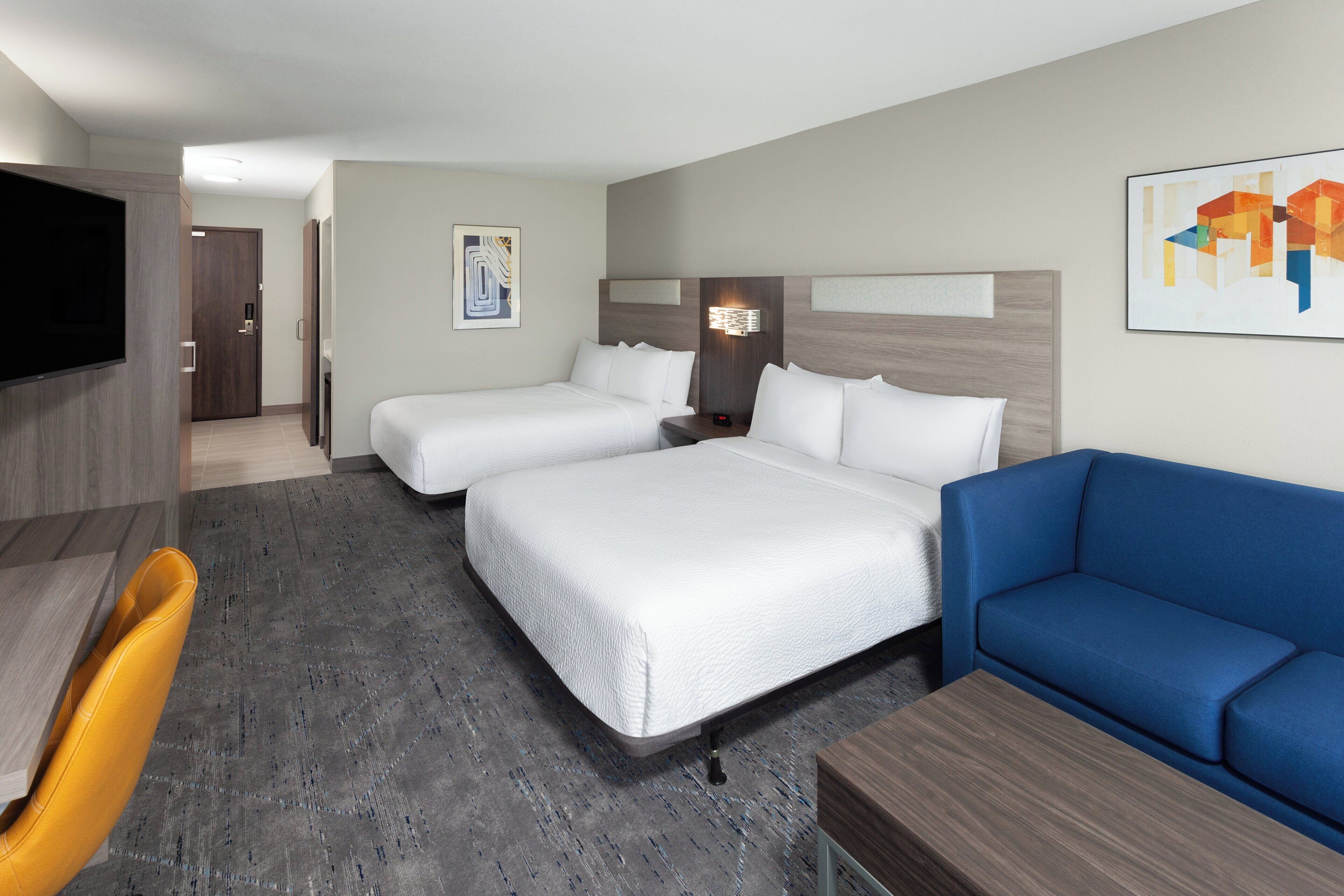 A hotel room with two beds, a blue sofa, a wooden desk, and a flat-screen TV.