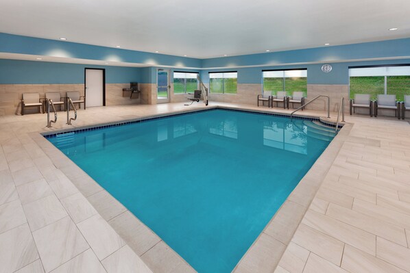 A large indoor swimming pool with clear blue water, surrounded by beige tiles and blue walls.