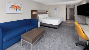 Une chambre d’hôtel avec un lit, un canapé bleu, une table basse en bois, un bureau avec une chaise jaune et un téléviseur fixé au mur.