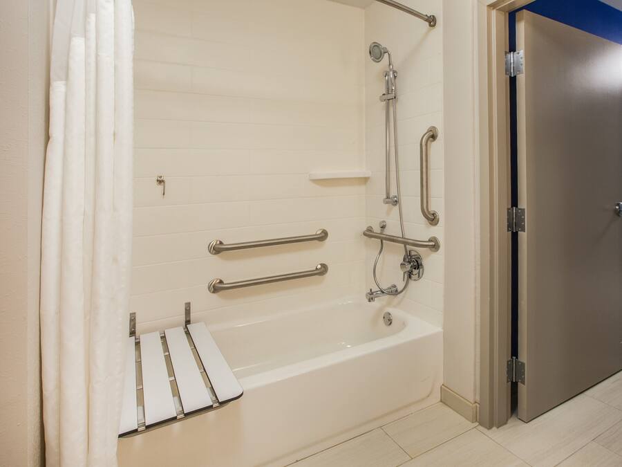 Un baño con bañera, barras de apoyo, cabezal de ducha y una puerta.