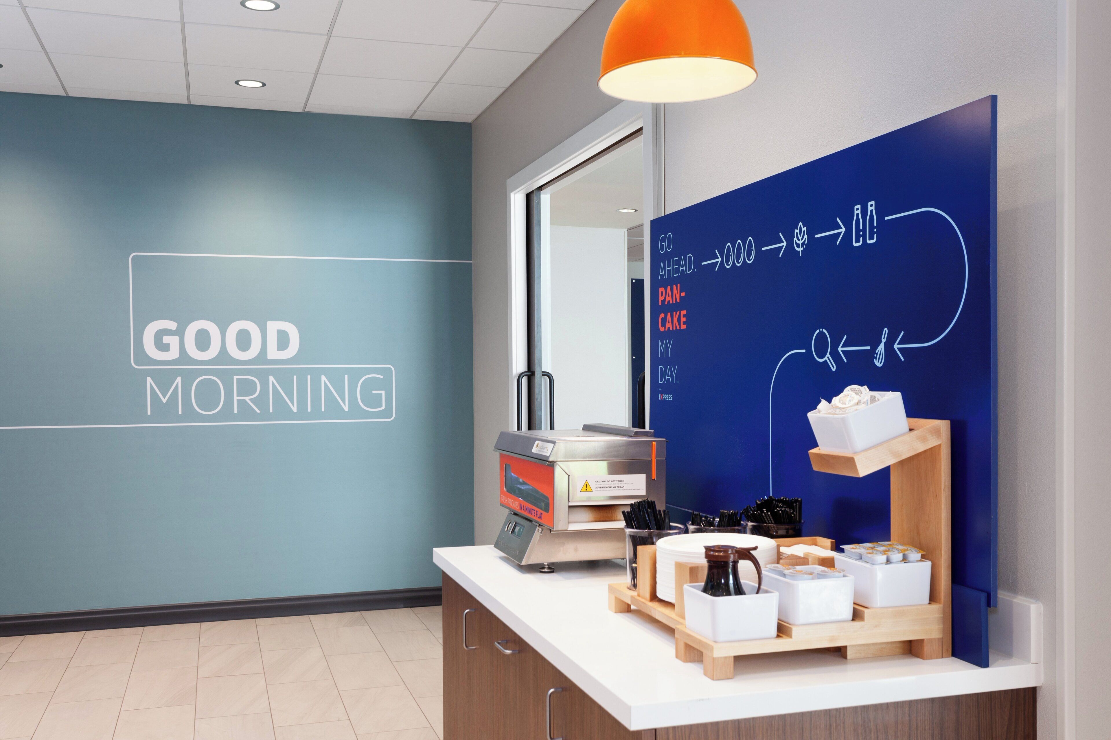 Un área de desayuno moderna con una pared azul, una máquina de café y una barra con diversas opciones para el desayuno.