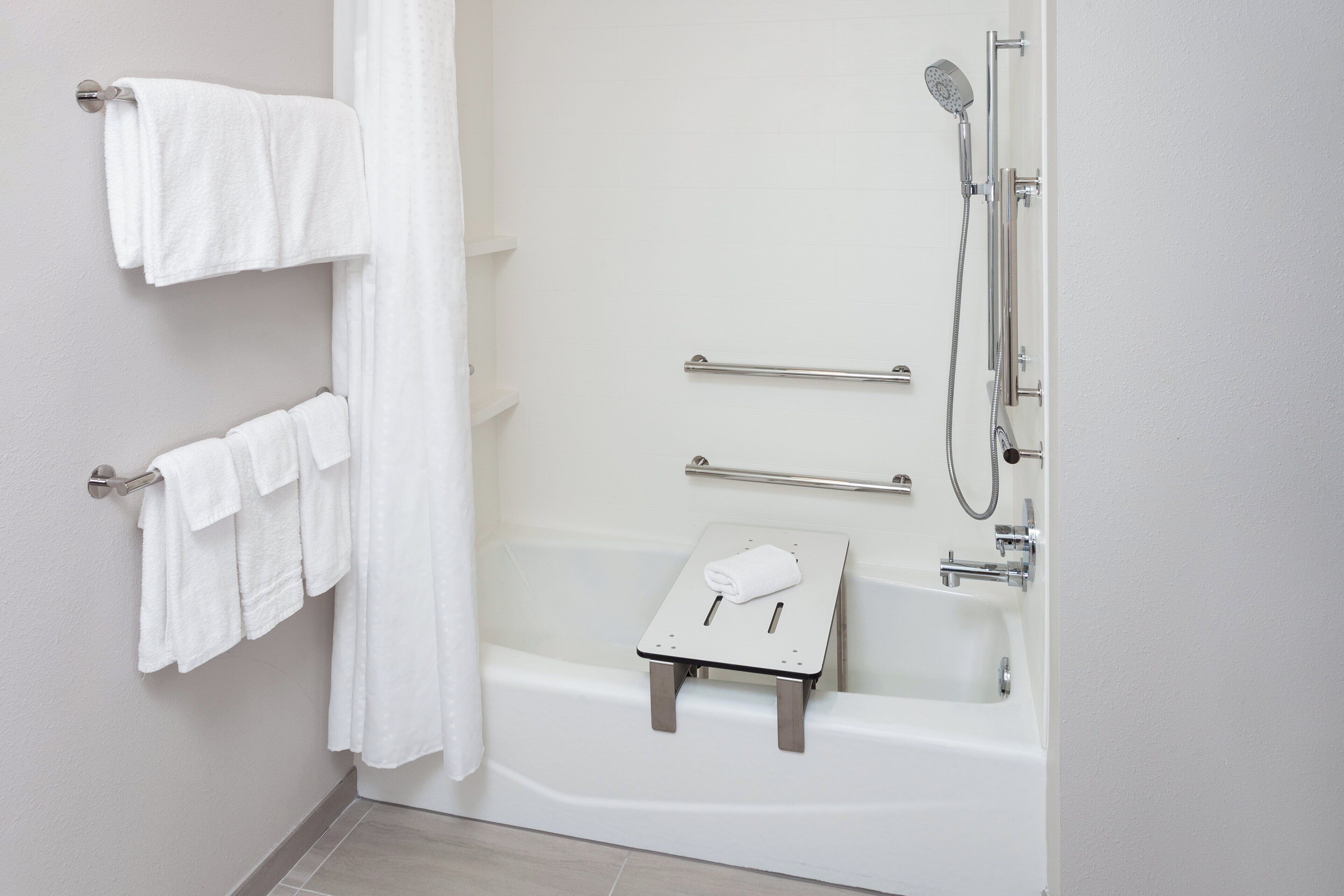 Een moderne badkamer met een badkuip, douche en een klein krukje met een handdoek.