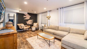 Ein modernes Wohnzimmer mit Sofa, Sesseln, einem Couchtisch und einer Wand mit einem Vogel-Wandbild.