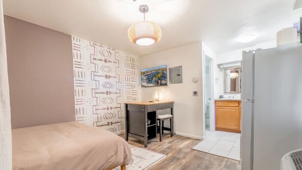 A compact bedroom with a bed, a desk, and a kitchenette. - Modern Haven: Chic Studio Getaway (Reno)