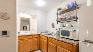 A modern kitchen with wooden cabinets, a microwave, a sink, and a shelf with kitchen utensils. - Modern Haven: Chic Studio Getaway (Reno)