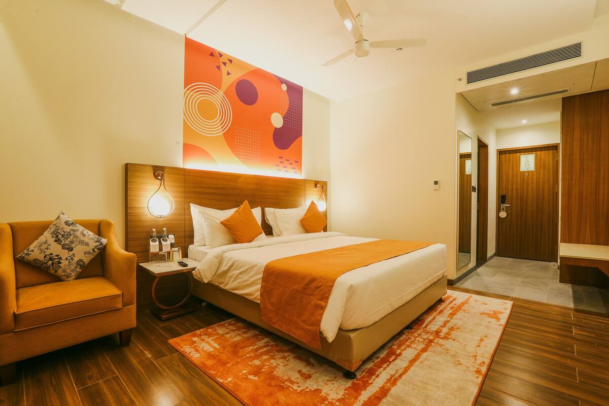 A hotel room with a bed, a sofa, a nightstand, and a wall art piece.