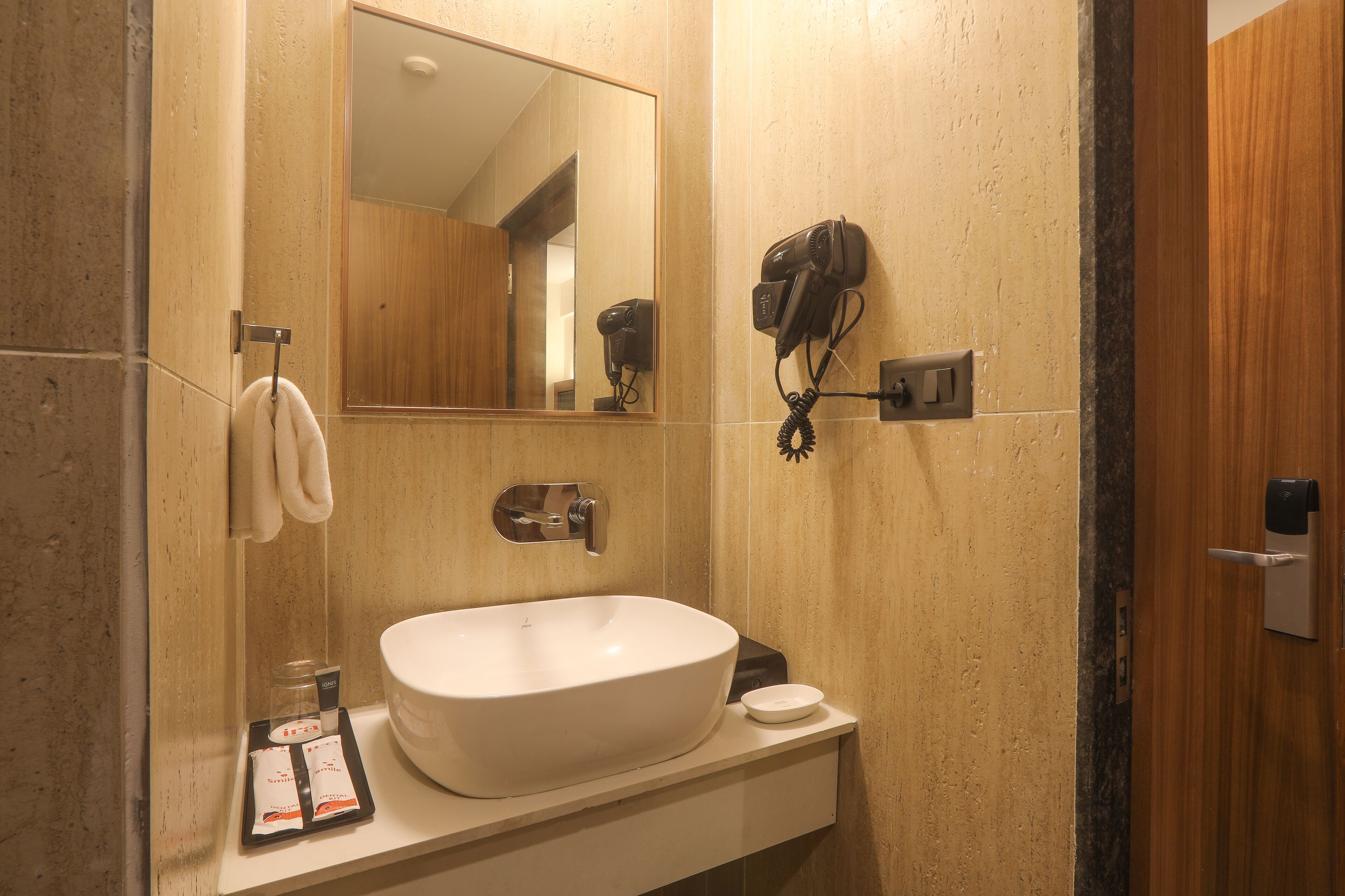 A bathroom with a white sink, a hairdryer mounted on the wall, a towel hanging on a rack, and a mirror above the sink.