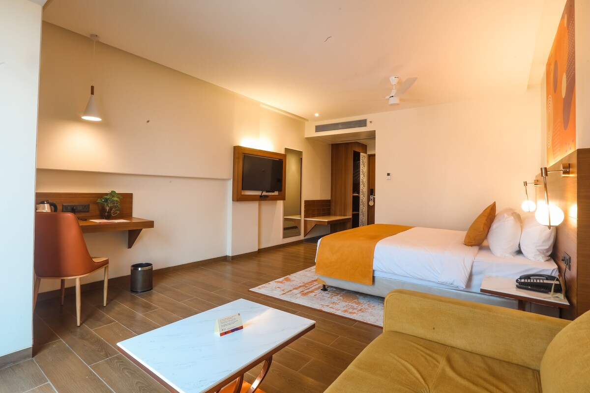 Habitación de hotel con una cama, un escritorio con una silla, una mesita y un televisor.