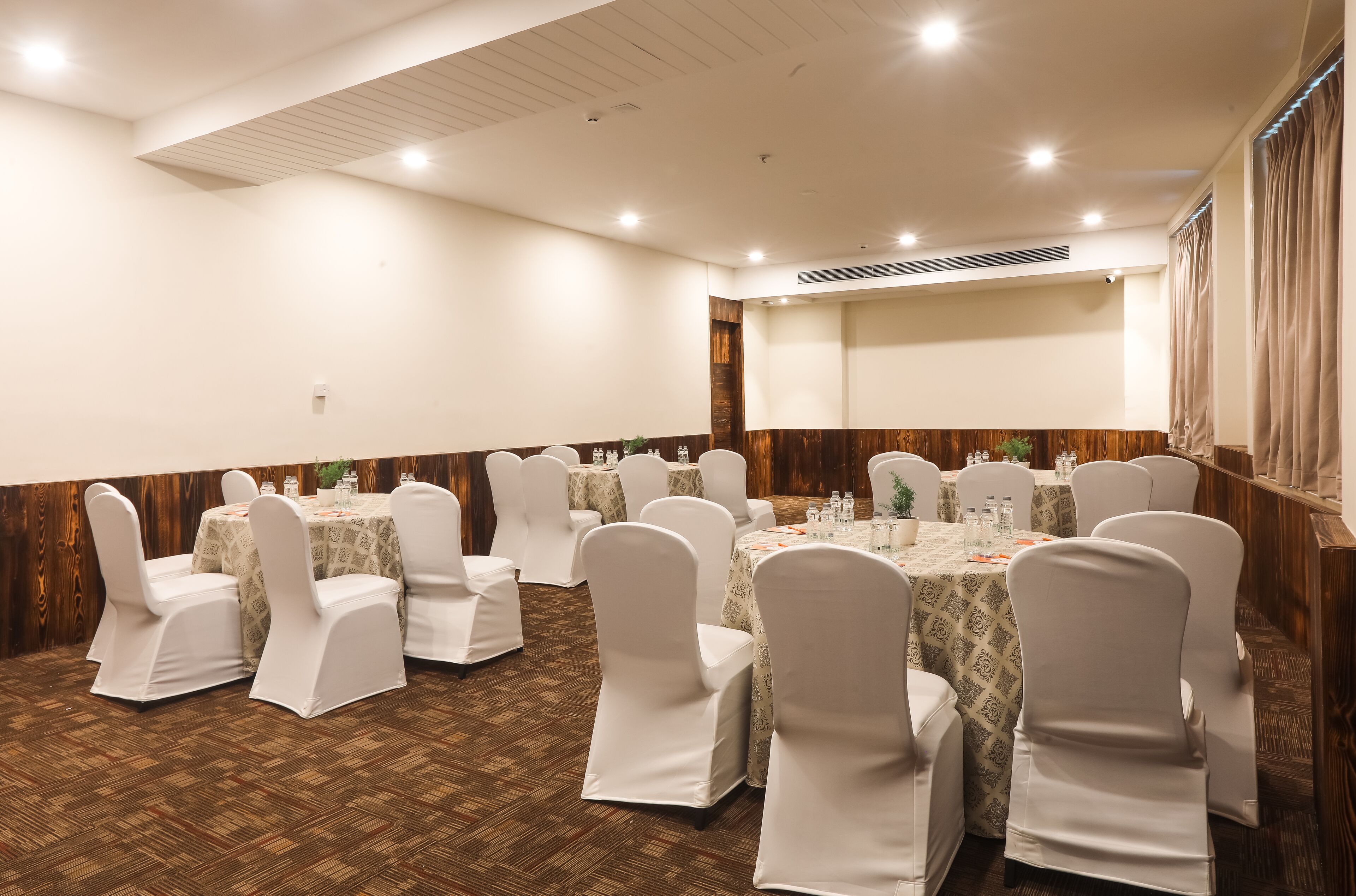 A conference room with round tables and white chairs, wooden paneling on the walls, and a patterned carpet.
