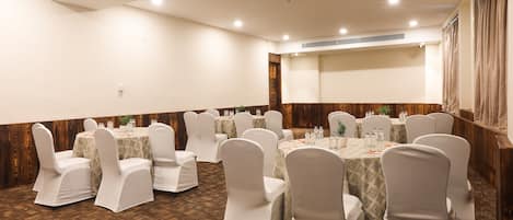A conference room with round tables and white chairs, wooden paneling on the walls, and a patterned carpet.