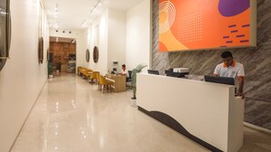 A hotel reception area with a marble reception desk, a large abstract wall art, and a seating area with chairs. - IRA by Orchid Sambhajinagar - Aurangabad (Chhatrapati Sambhajinagar)