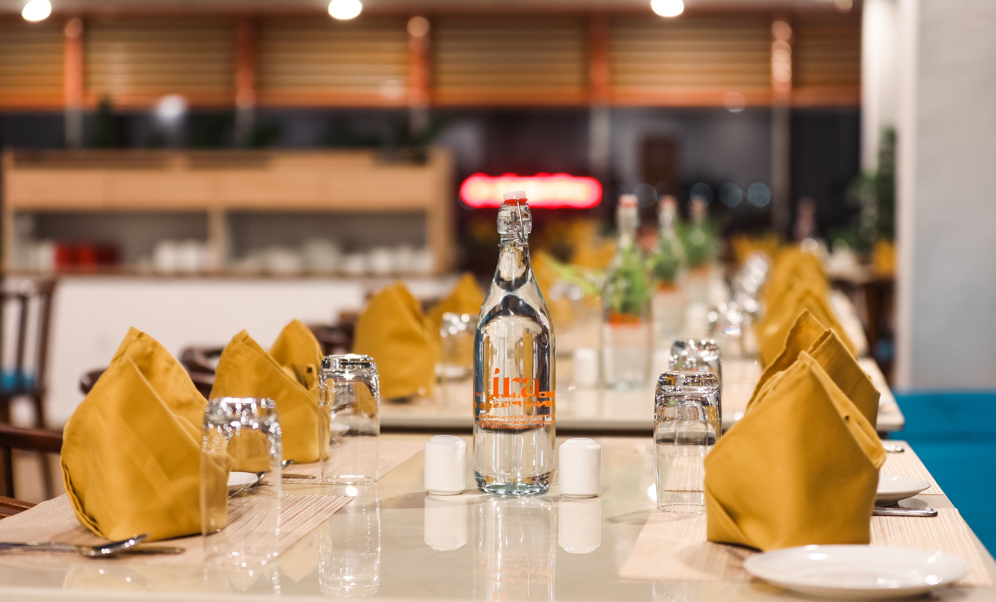 A restaurant setting with a table set for dining, featuring a bottle of liquor, glasses, and napkins.