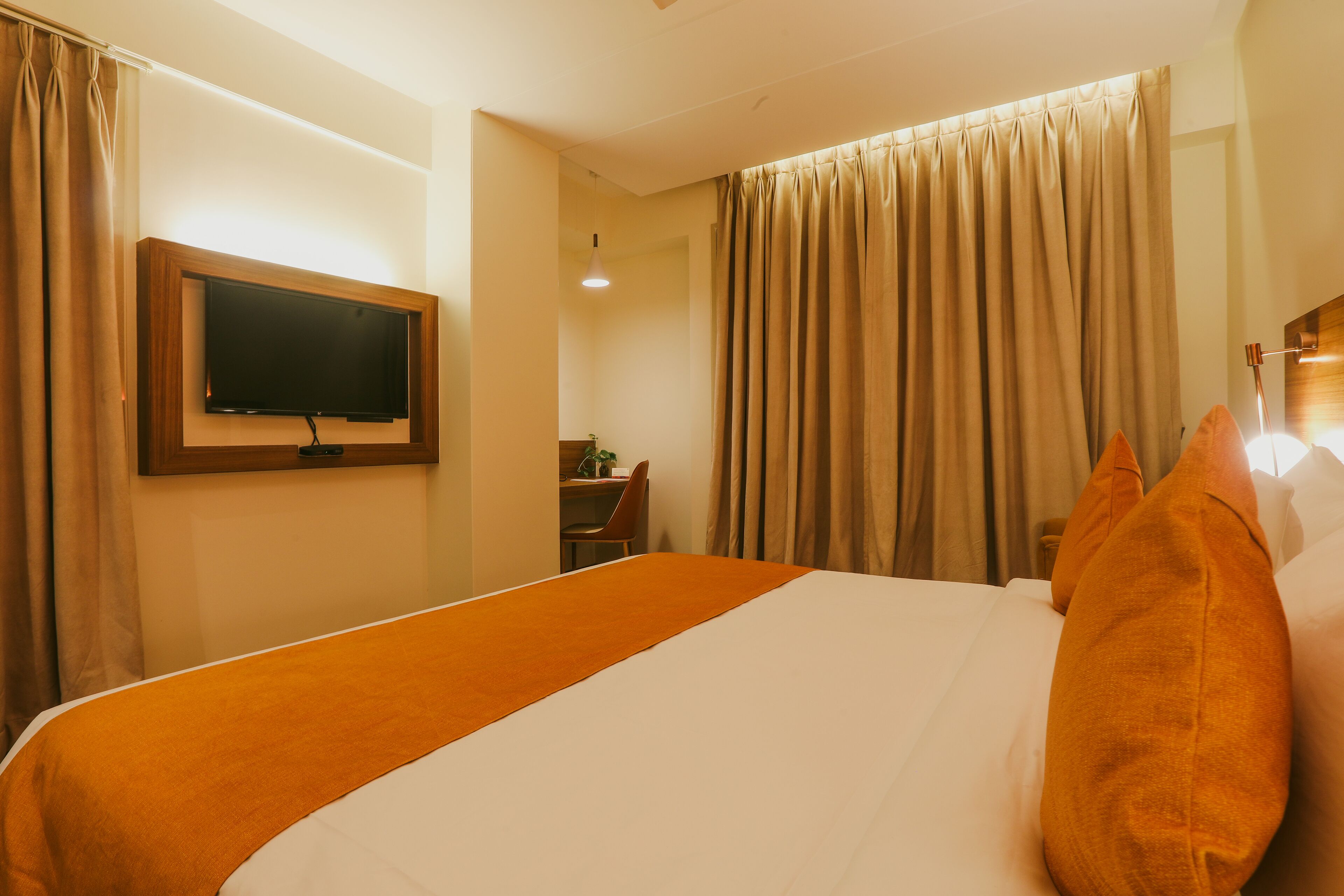 Una habitación de hotel con una cama grande, un televisor de pantalla plana en la pared, un escritorio con una silla y una ventana con cortinas.