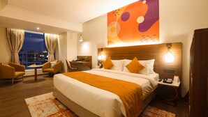A modern hotel room with a large bed, two bedside tables, a desk, and a view of the city at night. - IRA by Orchid Sambhajinagar - Aurangabad (Chhatrapati Sambhajinagar)