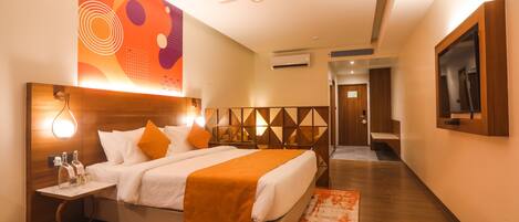 A modern hotel room with a large bed, a nightstand with a lamp, a ceiling fan, and a wall-mounted TV.