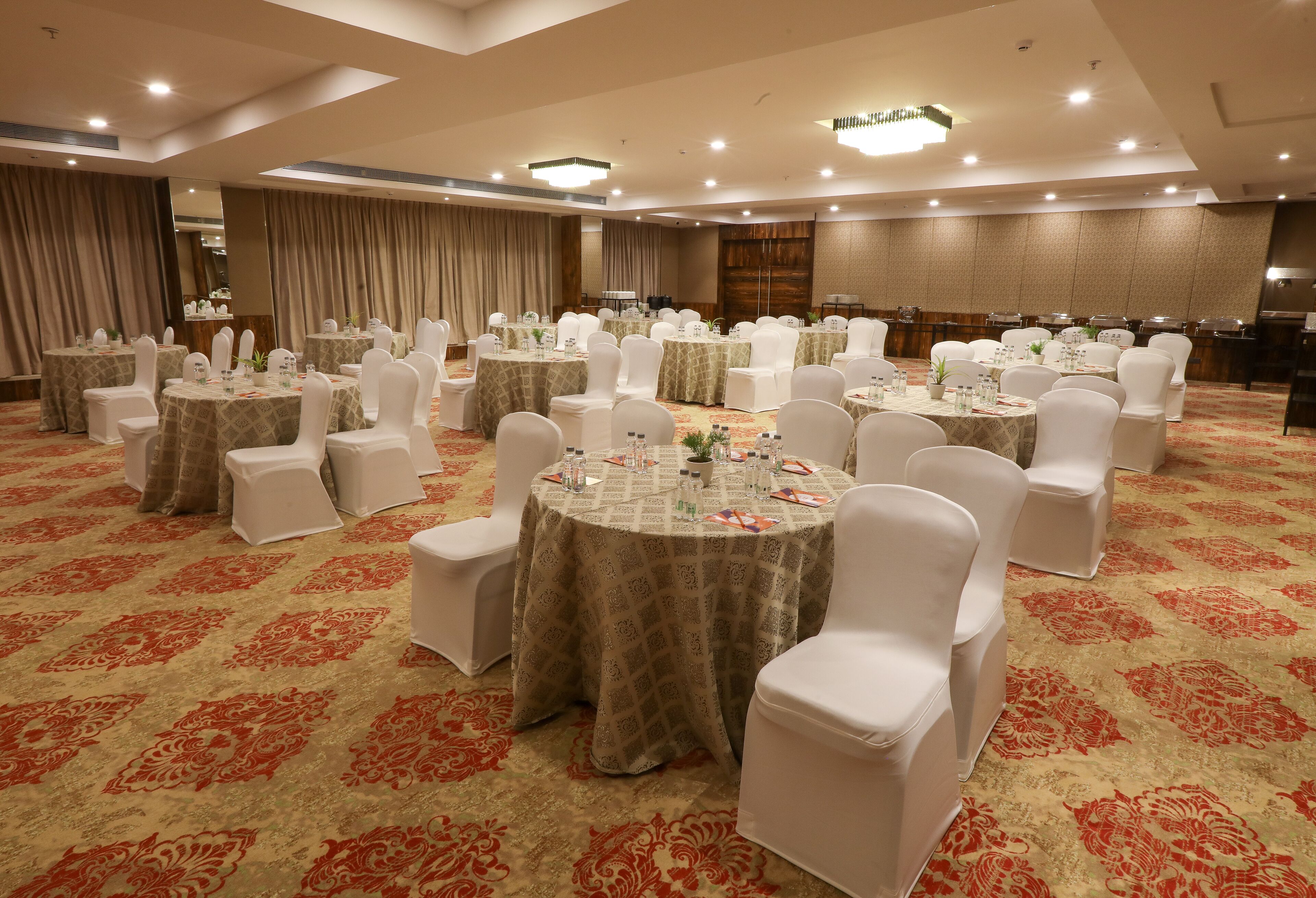 Un salón de banquetes con mesas redondas, sillas blancas y centros de mesa florales.