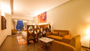 A modern living room with a sofa, armchairs, and a coffee table. There is a decorative wall piece and a view of the outside through a window. - IRA by Orchid Sambhajinagar - Aurangabad (Chhatrapati Sambhajinagar)