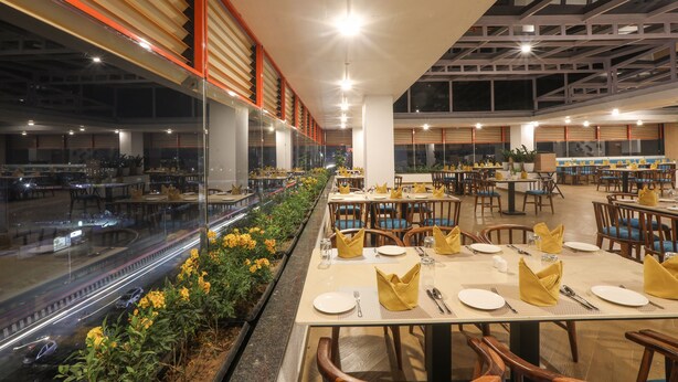 A spacious dining area with tables set for service, large windows along the walls, and a view of the cityscape. - IRA by Orchid Sambhajinagar - Aurangabad (Chhatrapati Sambhajinagar)