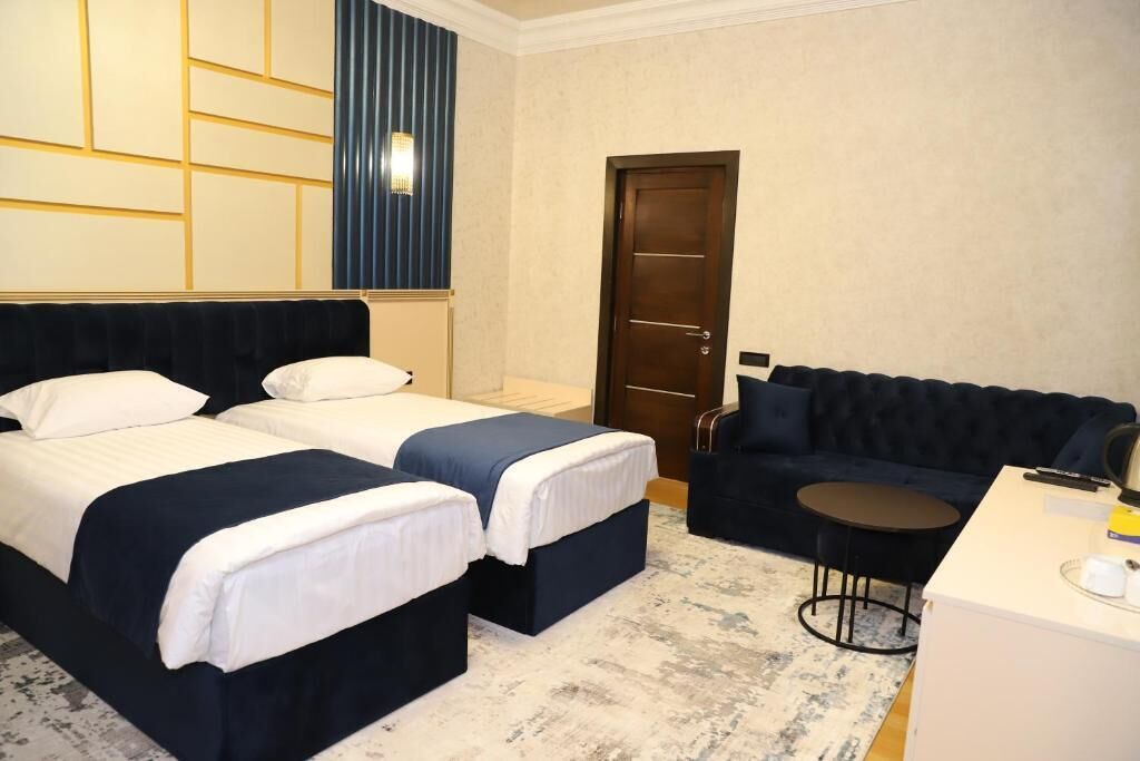 A hotel room with two beds, a dark blue sofa, a small round table, and a white desk.