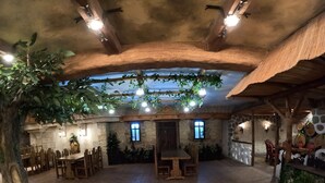 A rustic dining area with wooden tables and chairs, stone walls, and hanging plants.