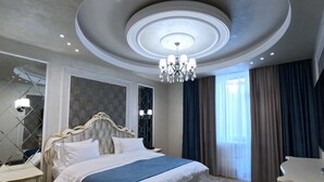 A spacious bedroom with a large bed, a chandelier, a nightstand, and a dresser.