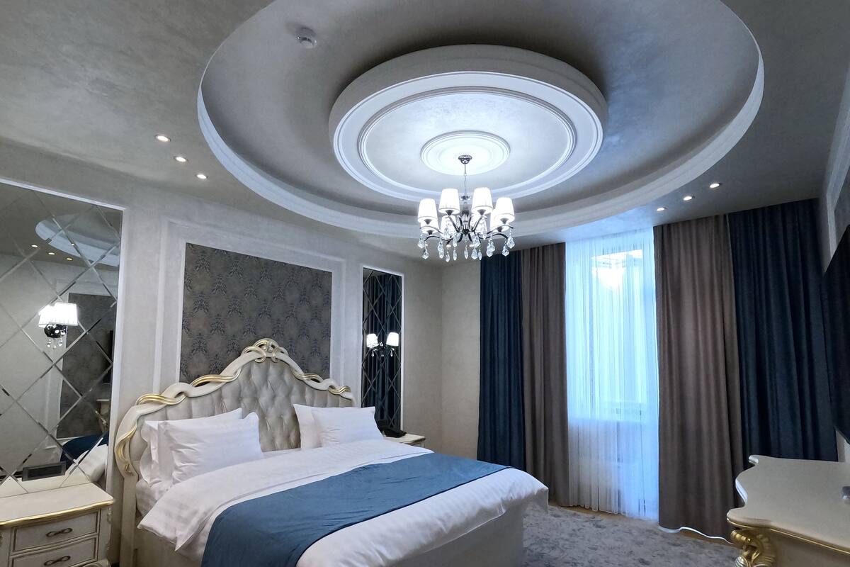 A spacious bedroom with a large bed, a chandelier, a nightstand, and a dresser.