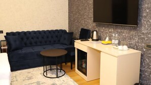 A modern room with a dark blue sofa, a small round table, a white cabinet with a flat-screen TV mounted above it, and a coffee maker on the cabinet.