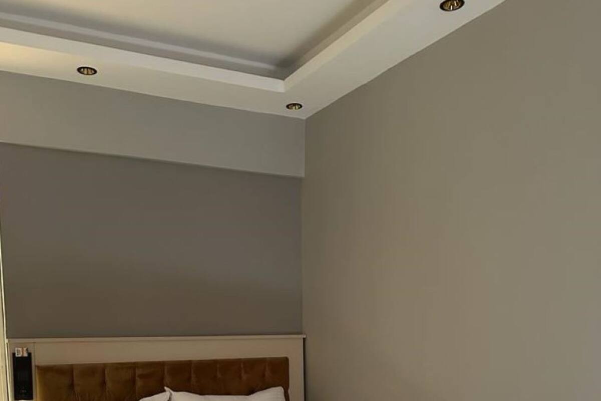 Un lit bien fait, avec du linge de lit blanc et une tête de lit marron, dans une chambre d’hôtel.