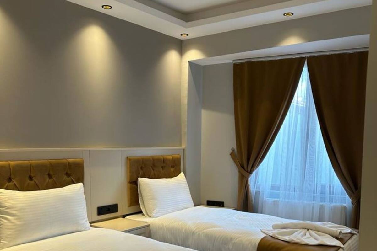 Une chambre d’hôtel avec deux lits, chacun doté d’une tête de lit, d’une grande fenêtre avec des rideaux et d’un plancher en bois.