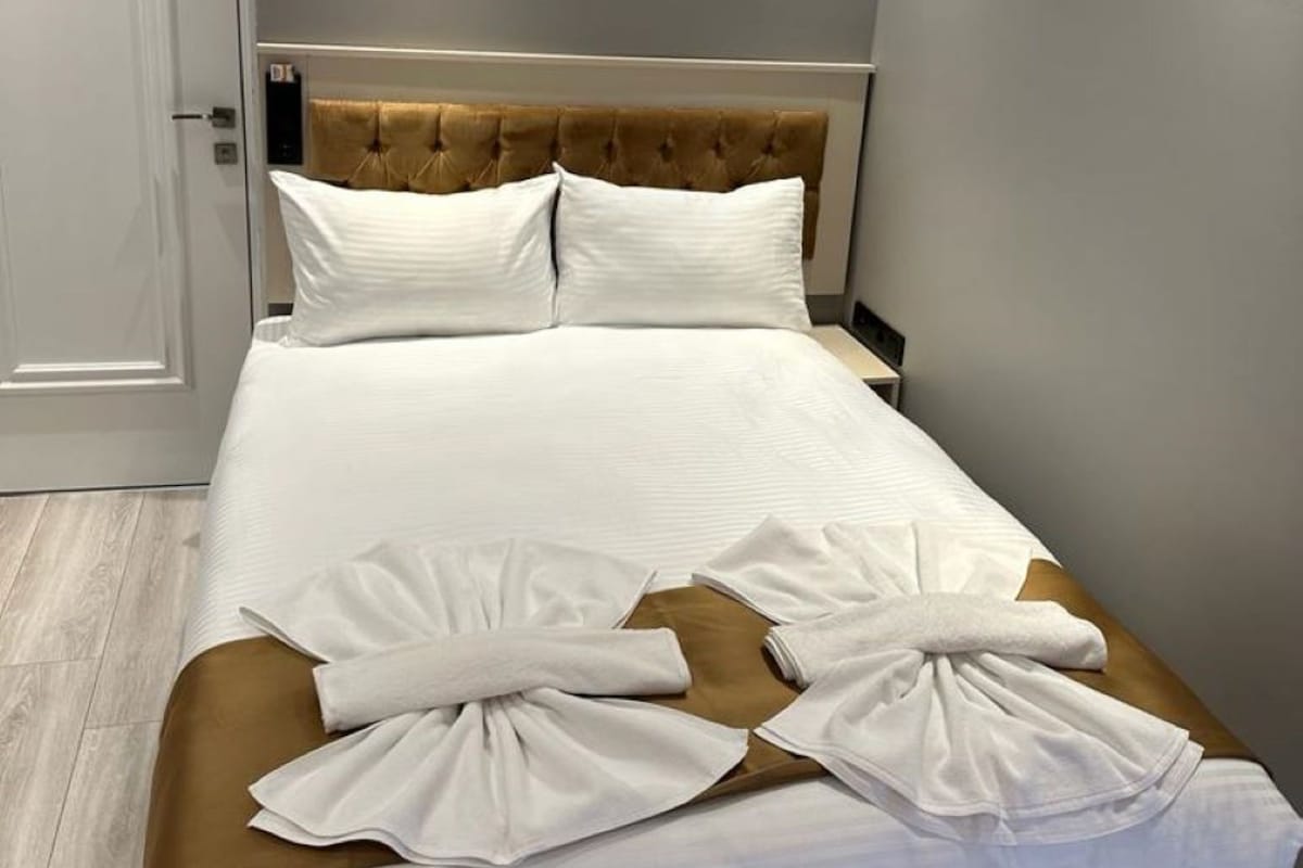 A neatly made bed with white linens and two pillows, a brown headboard, and a pair of towels on the footboard.
