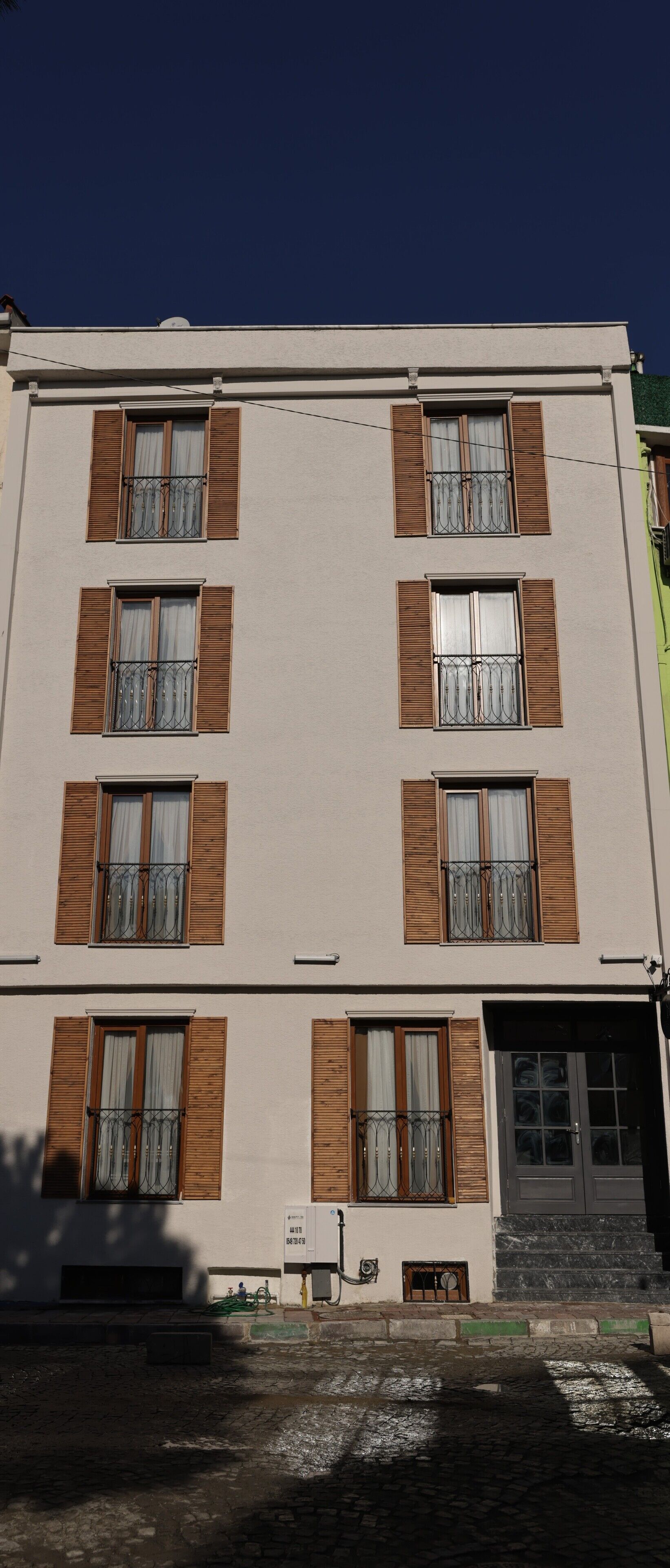 A multi-story building with a flat facade, evenly spaced windows with wooden shutters, and a ground-level entrance with steps.