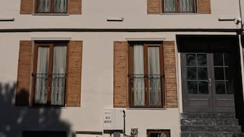 A multi-story building with a flat facade, evenly spaced windows with wooden shutters, and a ground-level entrance with steps.