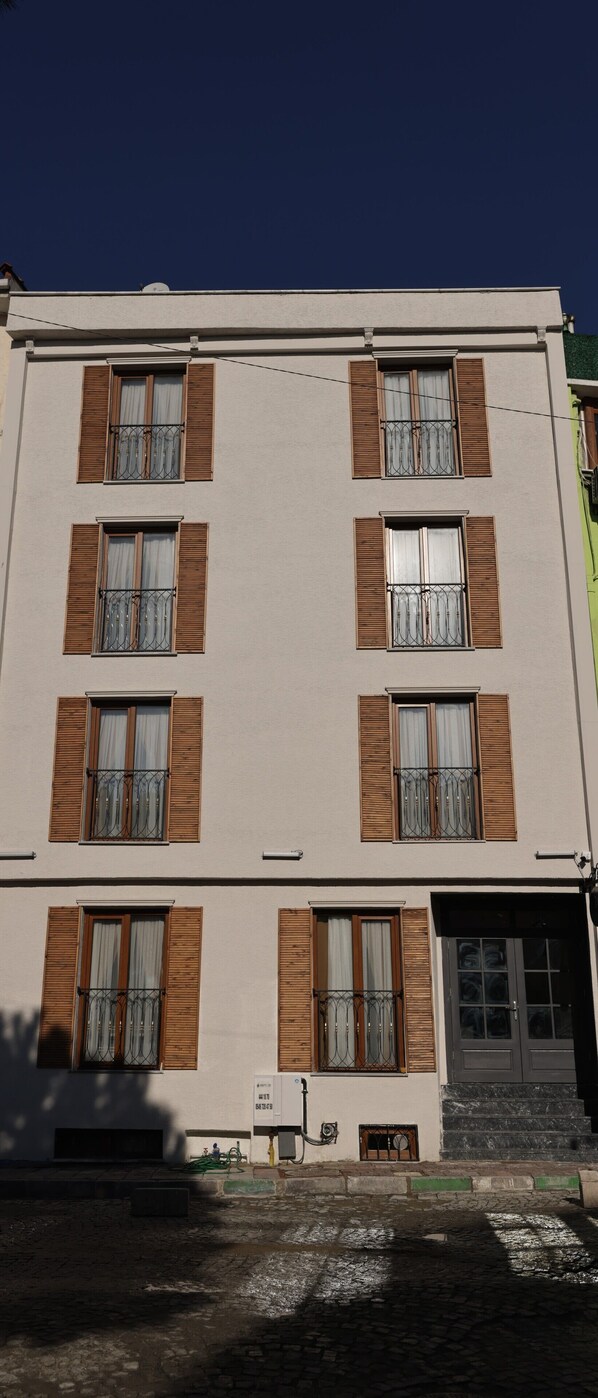 A multi-story building with a flat facade, evenly spaced windows with wooden shutters, and a ground-level entrance with steps.